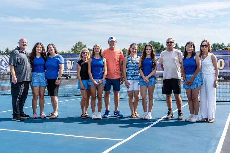 A group photo of the Poland Seminary High School Girls Tennis 2026 Seniors with their parents on the tennis courts. A blue Bulldogs backdrop drapes the fence behind them.