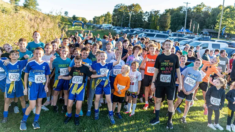 A large group of people in a grass field with running bibs on before running in the Zombie Run at Poland Township Park.